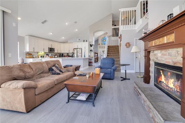 living area with light wood finished floors, visible vents, stairway, a fireplace, and high vaulted ceiling