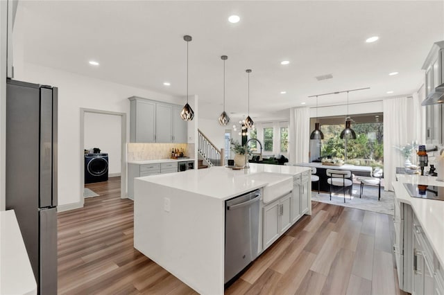 kitchen featuring sink, hanging light fixtures, stainless steel appliances, an island with sink, and washer / clothes dryer