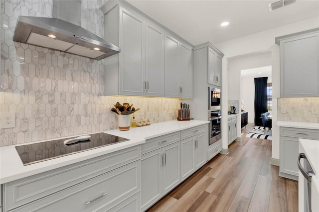 kitchen with black electric stovetop, wall chimney range hood, light hardwood / wood-style floors, and decorative backsplash