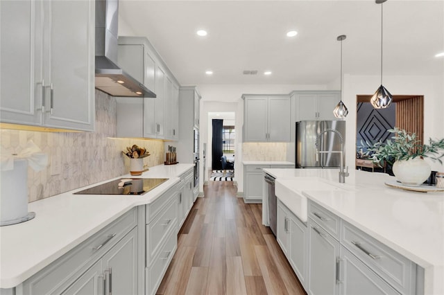 kitchen featuring pendant lighting, sink, appliances with stainless steel finishes, wall chimney exhaust hood, and light wood-type flooring