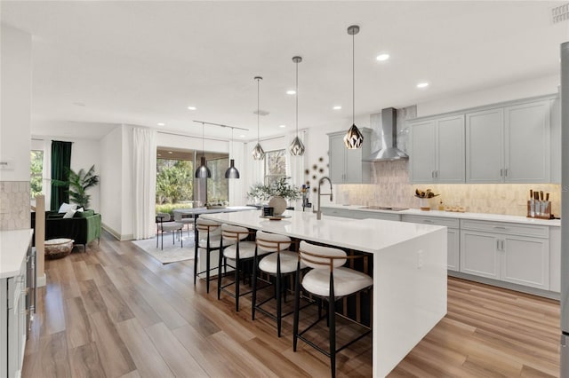 kitchen with a kitchen breakfast bar, black electric stovetop, a center island with sink, decorative light fixtures, and wall chimney exhaust hood