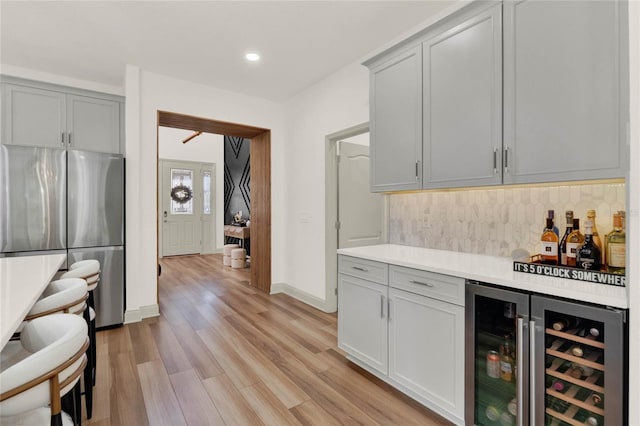 bar with stainless steel refrigerator, gray cabinetry, decorative backsplash, beverage cooler, and light wood-type flooring