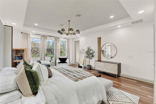 bedroom with light hardwood / wood-style flooring, a raised ceiling, and a chandelier