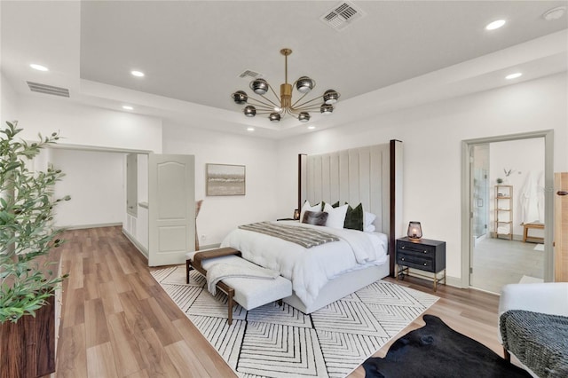 bedroom featuring a chandelier, a raised ceiling, and light hardwood / wood-style floors