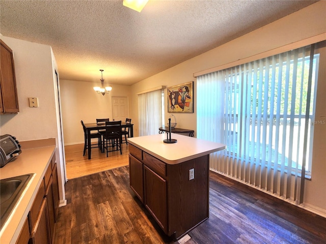 kitchen featuring pendant lighting, dark wood-type flooring, a healthy amount of sunlight, and a center island with sink