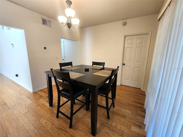 dining room with an inviting chandelier, light hardwood / wood-style floors, and a textured ceiling