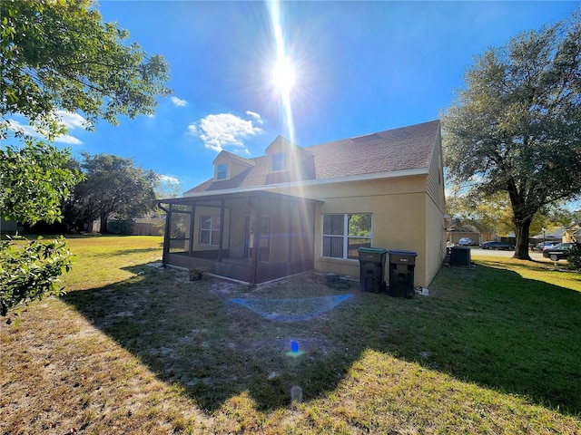 rear view of property with central AC, a sunroom, and a lawn