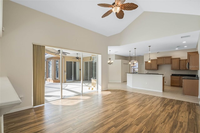 unfurnished living room featuring ceiling fan with notable chandelier, a wealth of natural light, and light hardwood / wood-style floors