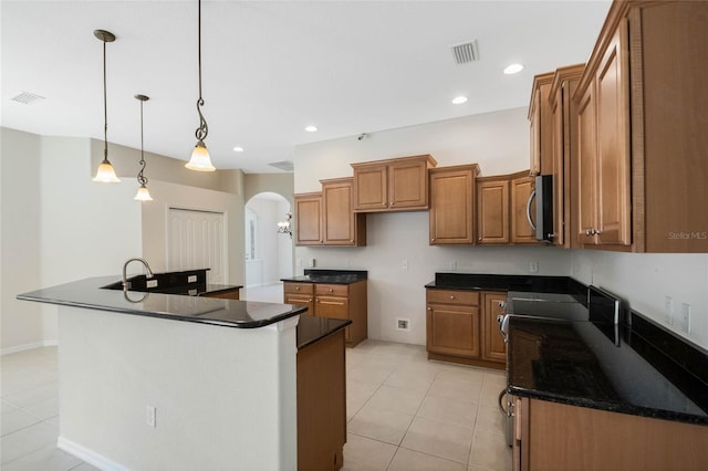 kitchen with pendant lighting, light tile patterned floors, an island with sink, and dark stone counters