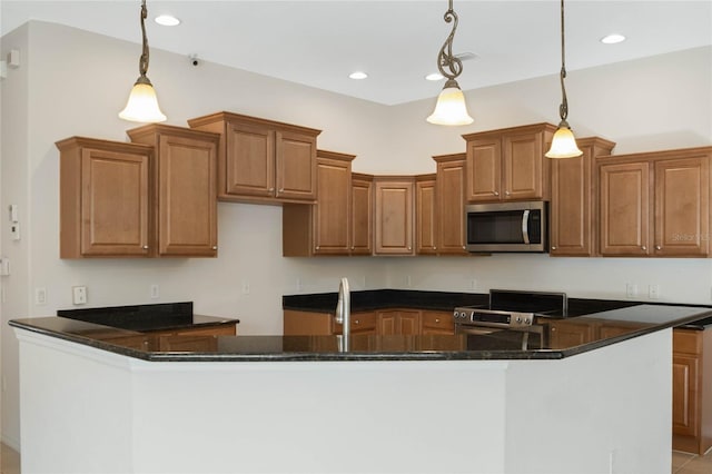 kitchen with dark stone countertops, hanging light fixtures, a kitchen island with sink, and appliances with stainless steel finishes