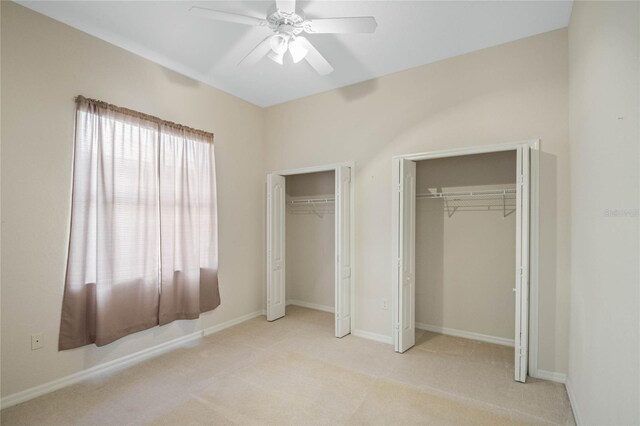 unfurnished bedroom with light carpet, two closets, and ceiling fan