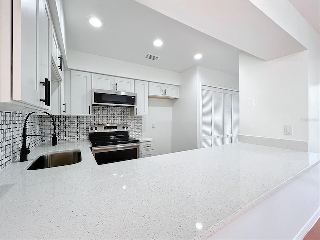 kitchen featuring sink, appliances with stainless steel finishes, backsplash, light stone countertops, and kitchen peninsula