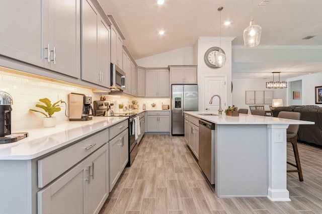 kitchen featuring gray cabinetry, stainless steel appliances, a breakfast bar, a sink, and pendant lighting