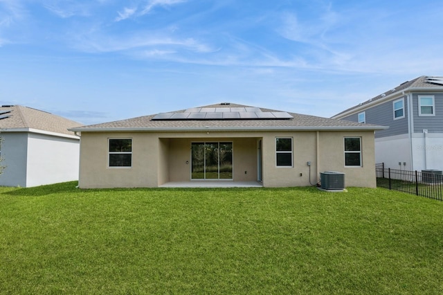 back of house with a yard, stucco siding, fence, and roof mounted solar panels