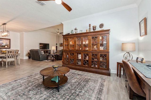 living area featuring baseboards, visible vents, light wood-style flooring, crown molding, and ceiling fan with notable chandelier