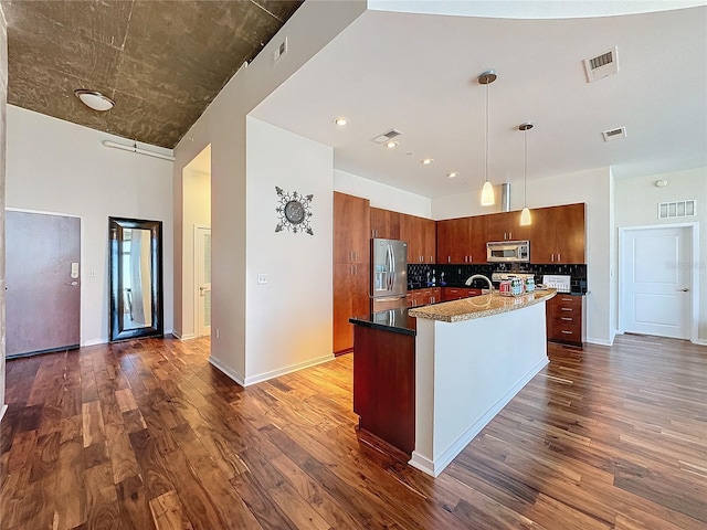 kitchen featuring dark wood-type flooring, stainless steel appliances, decorative light fixtures, and an island with sink