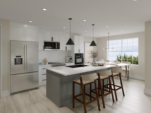 kitchen featuring sink, a center island with sink, stainless steel appliances, light stone countertops, and white cabinets