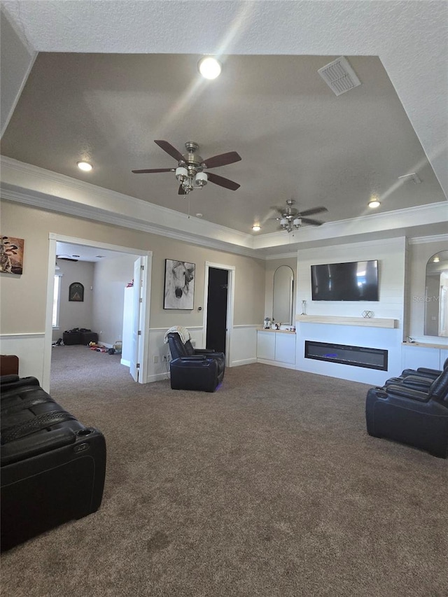 carpeted living room featuring ornamental molding, ceiling fan, a textured ceiling, and a tray ceiling