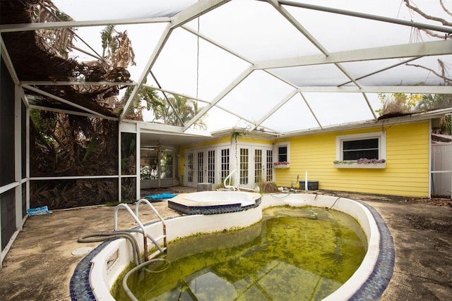 back of house with french doors, glass enclosure, a pool with hot tub, and a patio