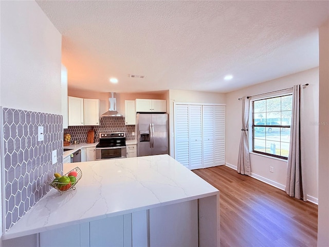 kitchen with wall chimney range hood, stainless steel appliances, kitchen peninsula, and white cabinets