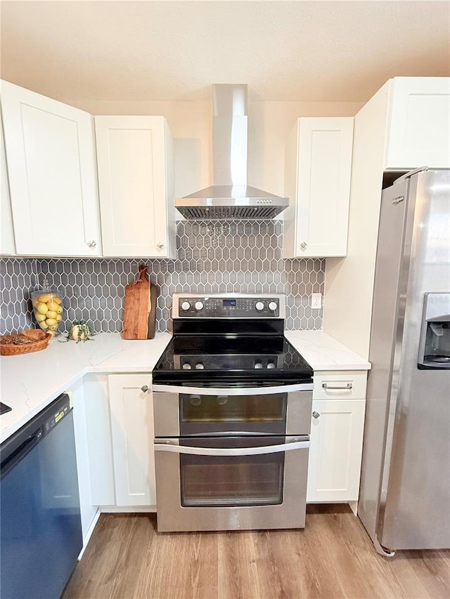 kitchen with white cabinetry, appliances with stainless steel finishes, wall chimney exhaust hood, and light hardwood / wood-style floors