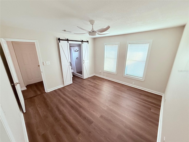 unfurnished bedroom with ceiling fan, dark hardwood / wood-style floors, a barn door, and a textured ceiling