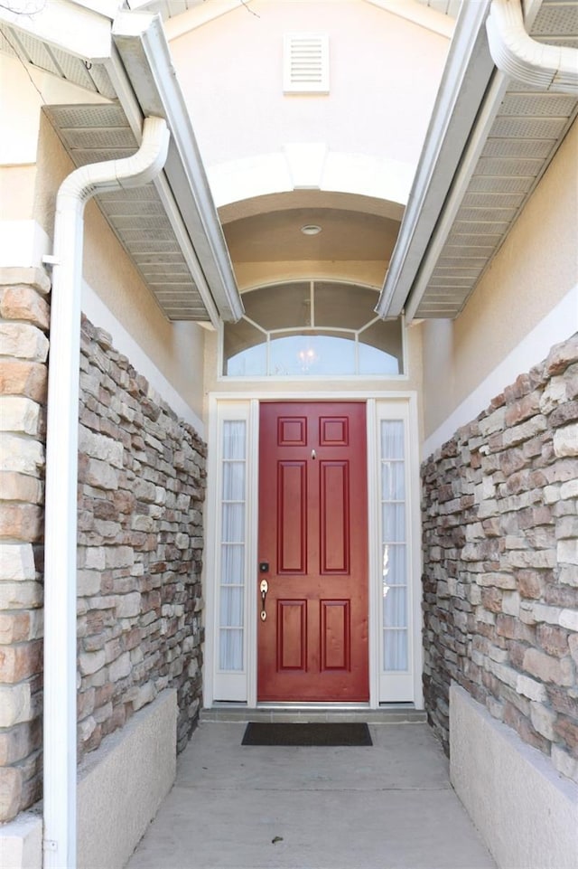 entrance to property featuring stone siding, visible vents, and stucco siding