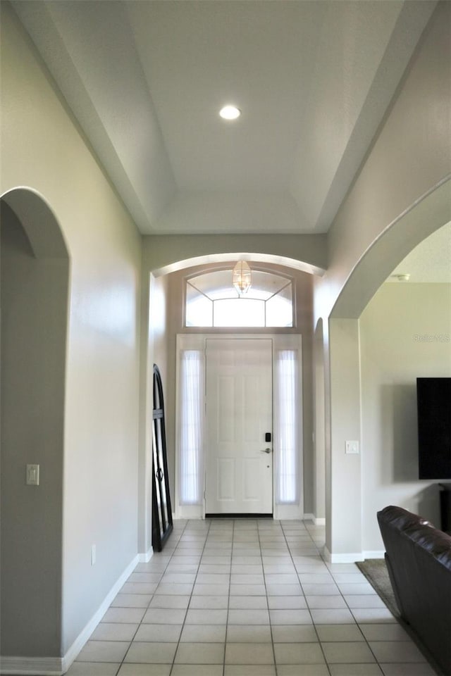 entrance foyer featuring arched walkways, a raised ceiling, light tile patterned flooring, and baseboards