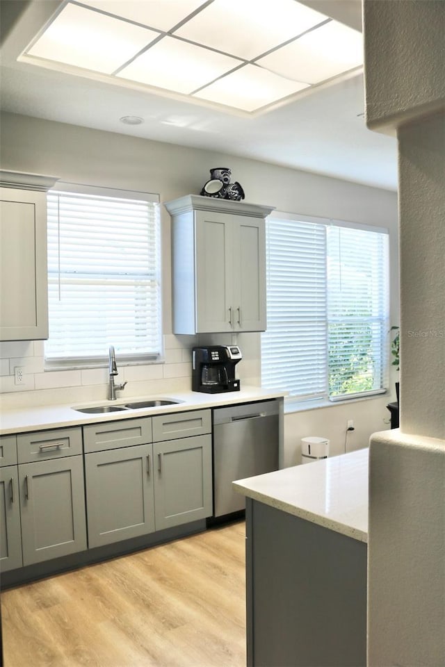 kitchen with tasteful backsplash, sink, stainless steel dishwasher, and light hardwood / wood-style floors