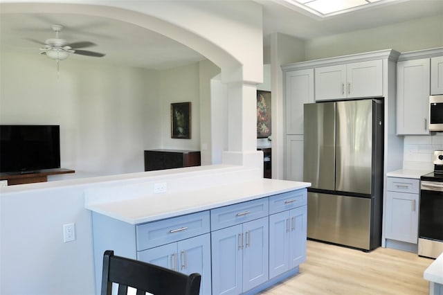 kitchen with appliances with stainless steel finishes, decorative backsplash, ceiling fan, and light hardwood / wood-style flooring