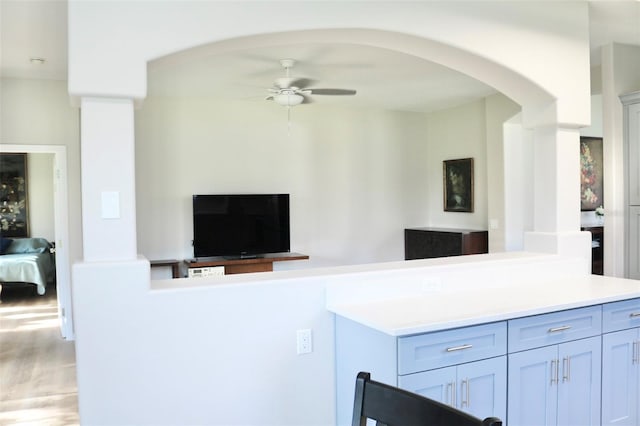 kitchen featuring arched walkways, a ceiling fan, open floor plan, wood finished floors, and light countertops