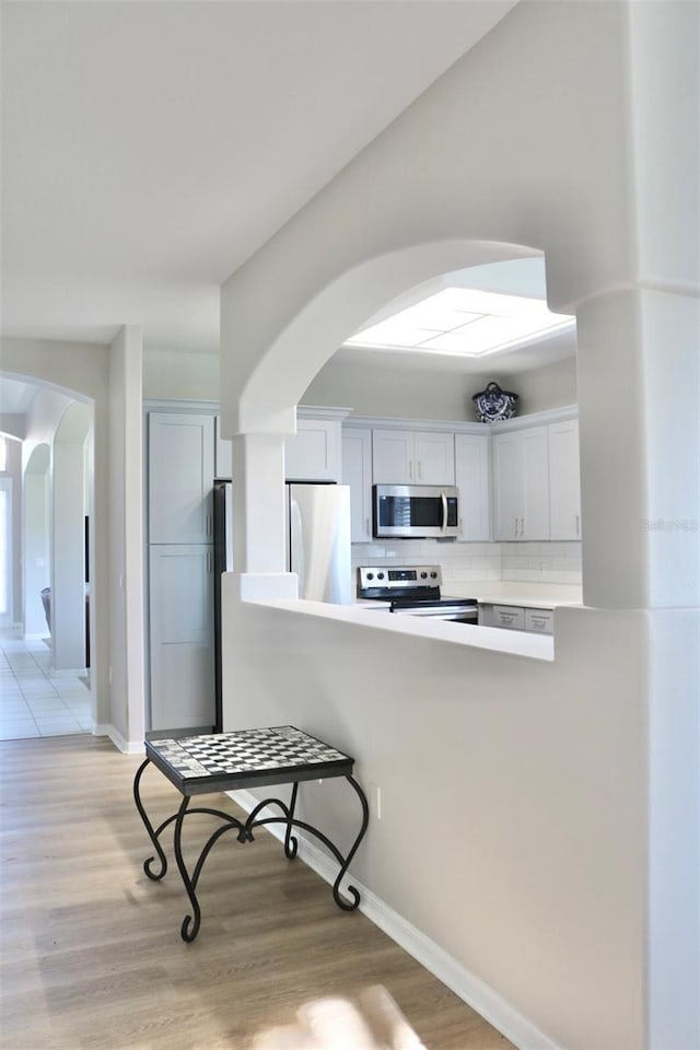 kitchen featuring backsplash, stainless steel appliances, light hardwood / wood-style floors, and white cabinets