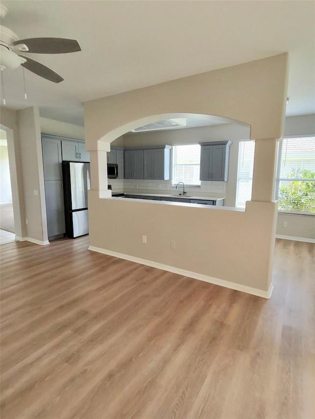 interior space featuring light wood finished floors, appliances with stainless steel finishes, a sink, gray cabinets, and backsplash