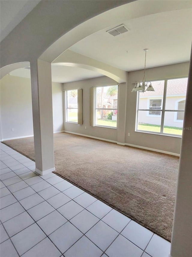 spare room featuring arched walkways, a notable chandelier, light colored carpet, visible vents, and baseboards