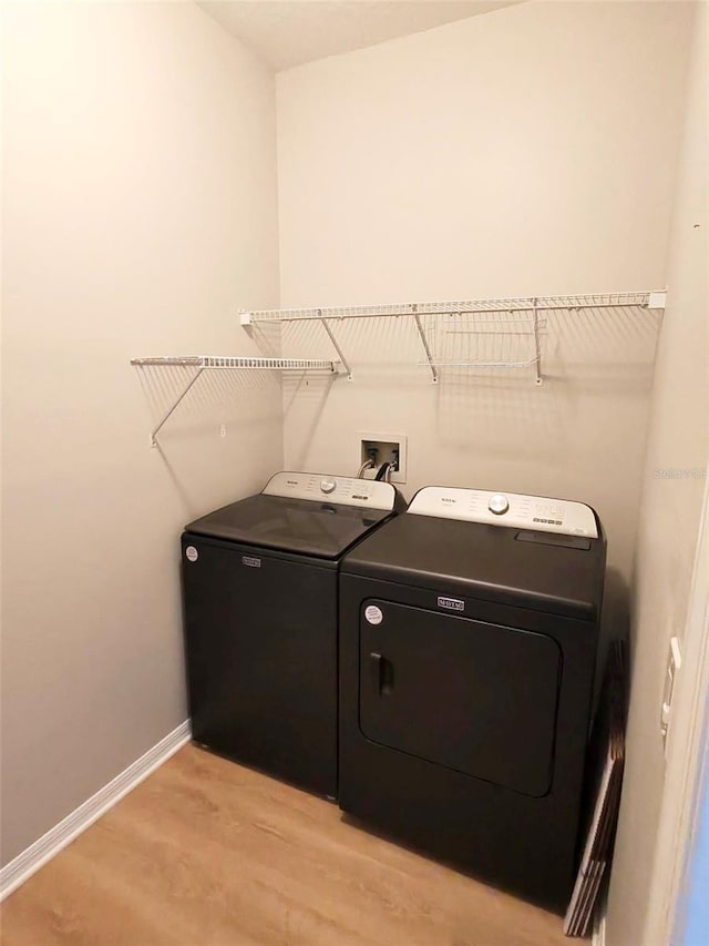 clothes washing area featuring light wood-style floors, washer and dryer, laundry area, and baseboards