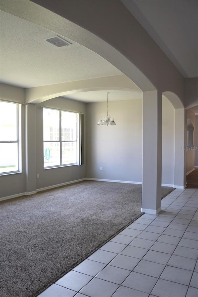 spare room featuring light carpet, arched walkways, visible vents, and a healthy amount of sunlight