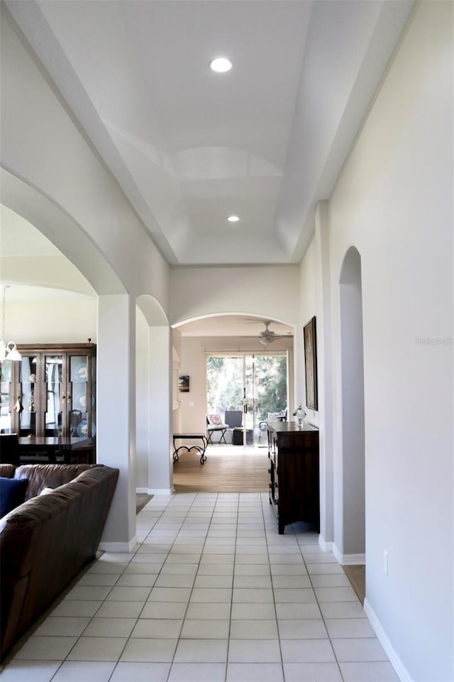 corridor featuring baseboards, arched walkways, a tray ceiling, light tile patterned flooring, and recessed lighting