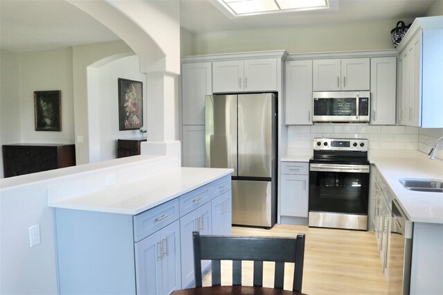 kitchen with light wood finished floors, stainless steel appliances, tasteful backsplash, light countertops, and a sink