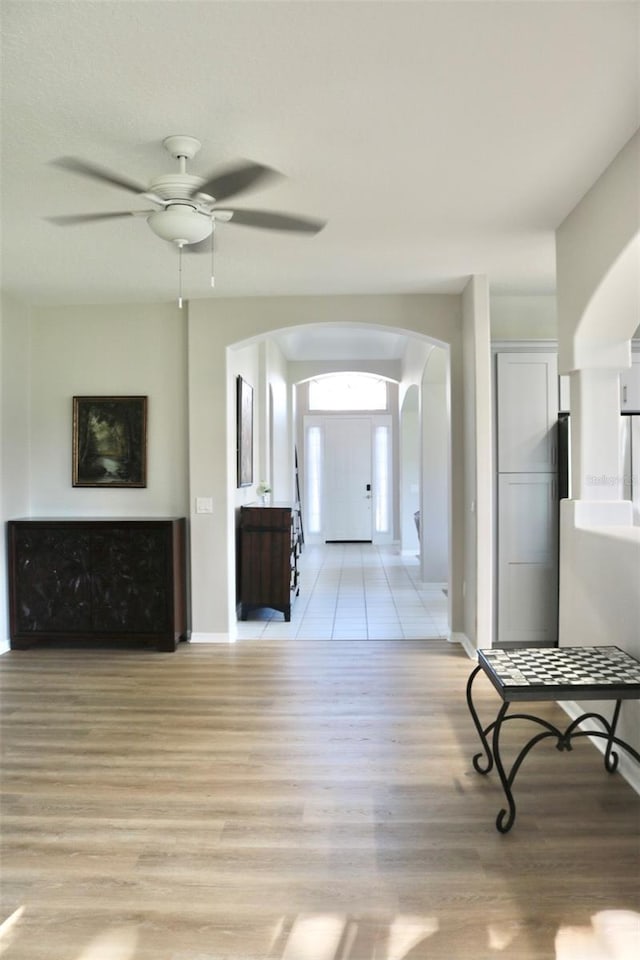 living area featuring arched walkways, ceiling fan, light wood-style flooring, and baseboards