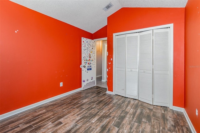 unfurnished bedroom with dark wood-type flooring, vaulted ceiling, a closet, and a textured ceiling