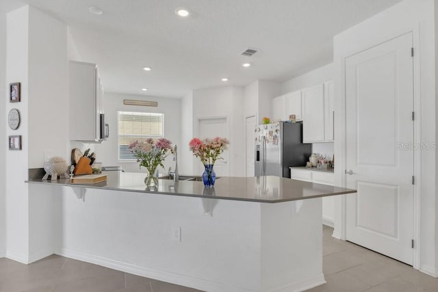 kitchen with sink, a kitchen breakfast bar, stainless steel refrigerator with ice dispenser, white cabinets, and kitchen peninsula