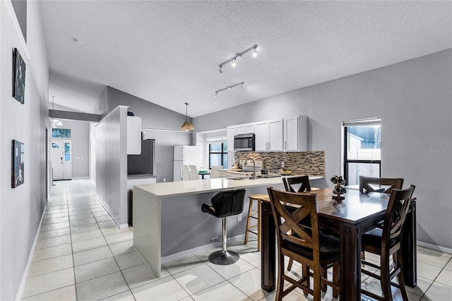 kitchen with vaulted ceiling, pendant lighting, white cabinetry, backsplash, and white fridge