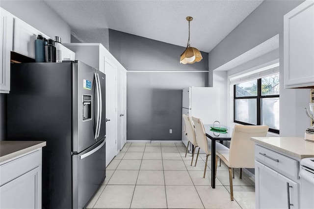 kitchen featuring vaulted ceiling, white cabinets, stainless steel fridge, hanging light fixtures, and light tile patterned floors