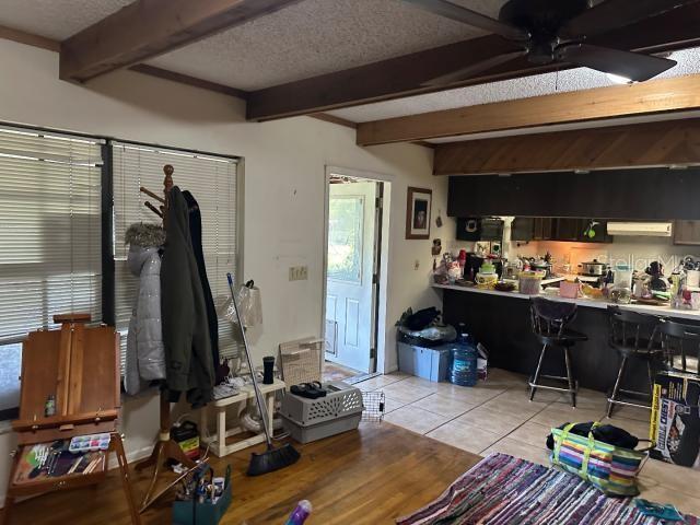 interior space with a textured ceiling, light tile patterned floors, a workshop area, ceiling fan, and beam ceiling