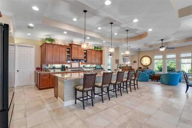 kitchen featuring a large island, hanging light fixtures, light stone countertops, a kitchen bar, and a raised ceiling