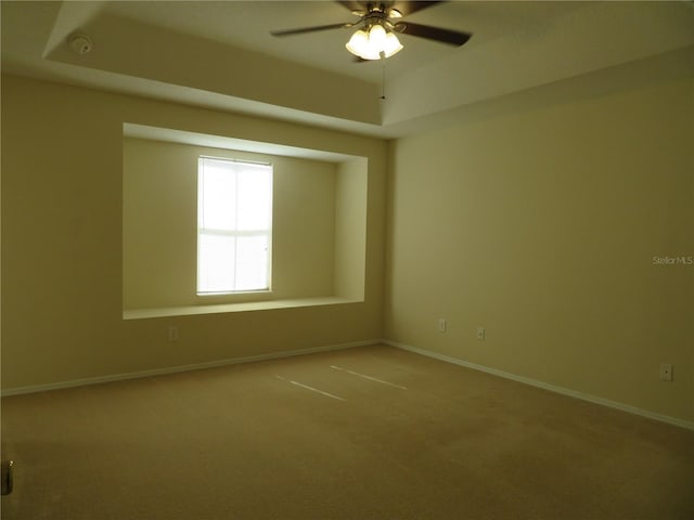 spare room with a tray ceiling, ceiling fan, and carpet