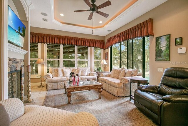 sunroom / solarium featuring visible vents, a stone fireplace, a tray ceiling, and a ceiling fan