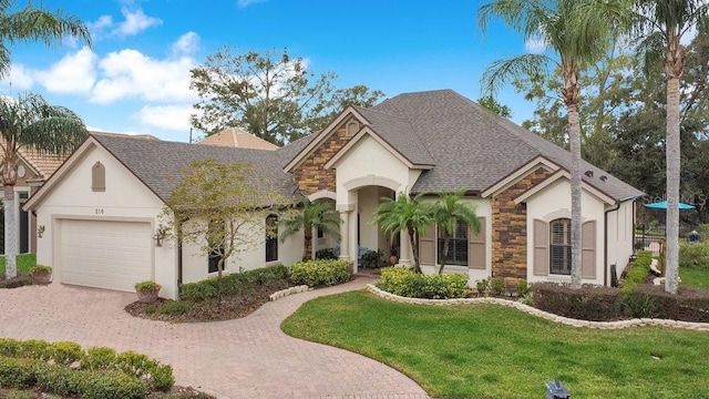 view of front of property with a garage, stone siding, roof with shingles, decorative driveway, and a front lawn