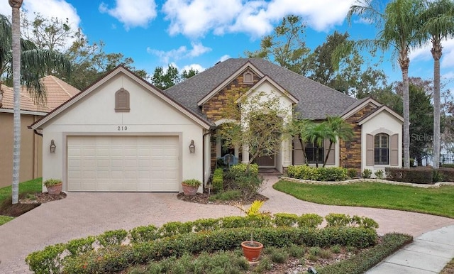 french country style house featuring an attached garage, driveway, stone siding, stucco siding, and a front yard