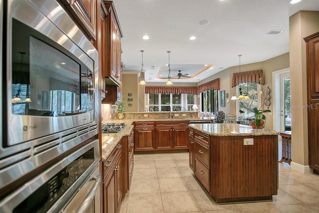 kitchen with stainless steel appliances, hanging light fixtures, a raised ceiling, and a center island